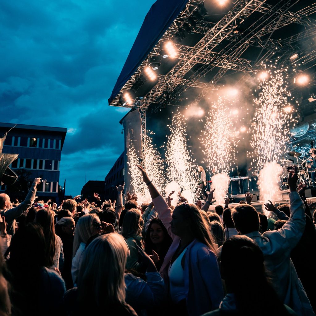 A Large Crowd At A Concert On A Bright Day With Firework